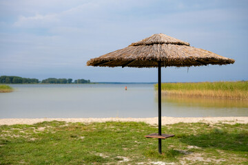 Umbrella beach of reed. Wild sandy beach on Svityaz Lake, Ukraine. Vacationers in the water in the distance.