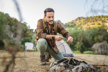 Adult man kneel and set up a campfire with sticks on camping trip