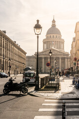 Visitors stroll along the street near the Pantheon in Paris, with its grand dome and classic architecture standing tall against the clear sky. It's a beautiful day filled with activity.
