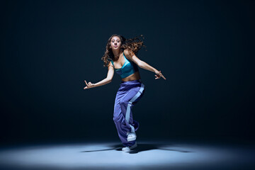 Dynamic image of young girl, dancer showing technique during focused hip hop training session against navy blue studio background. Concept of freestyle dance, modernity, urban culture, youth