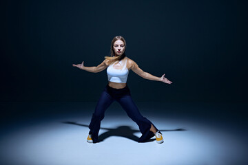 Obraz premium Youthful passion on display. Young energetic woman dancing hip hop with precision against navy blue studio background. Concept of freestyle dance, modernity, urban culture, youth