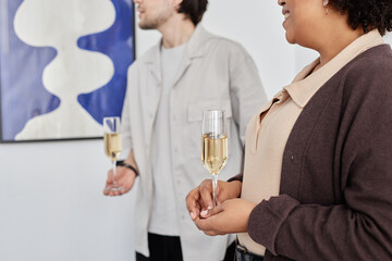 Cropped side view shot of two people holding champagne glasses and looking at paintings during art show opening ceremony, copy space