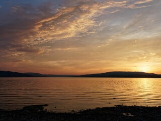 Sunset on a lake with mountains in the background and a sky covered with orange clouds