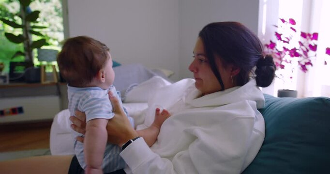 Mother lifts baby and smells the diaper to check for a possible diaper change, creating a realistic and relatable parenting moment in a cozy, home environment with natural light