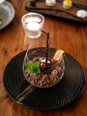 Chocolate dessert garnished with a raspberry and mint leaf, served in a glass on a black plate