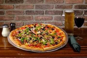 Vegetable pizza with beer and wine on a wooden table.