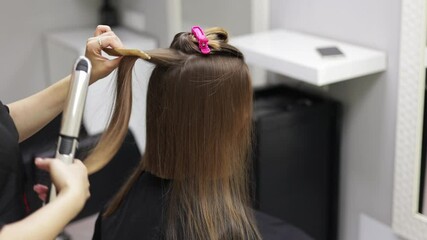 Unrecognisable professional hairdresser ironing female client hair with hair straightener and comb, making stylish hairstyle in beauty salon. Keratin, lamination,hair care, hair salon and hairstyling.