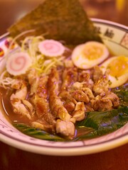 Close-up of a bowl of ramen with chicken and toppings.