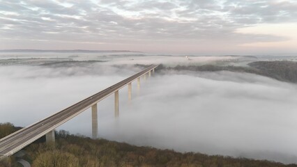 Stunning aerial view of a bridge extending over a foggy landscape with a cloudy sky