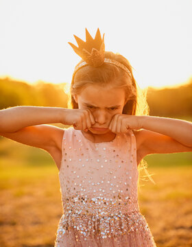 Sad, child and crying outdoor at sunset for bullying, stress or anxiety for trauma or crisis in summer. Depression, girl and tears of kid at park with crown, princess costume or upset to stop playing