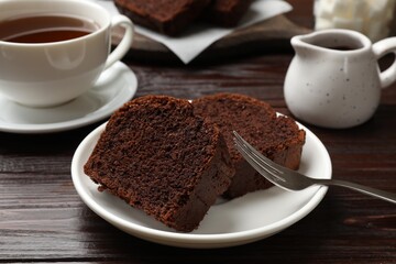 Slices of delicious chocolate sponge cake and tea on wooden table, closeup