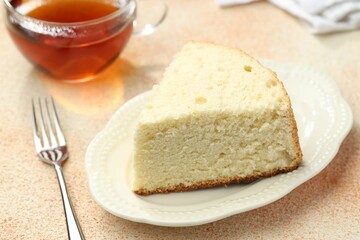 Piece of delicious sponge cake served on beige textured table, closeup
