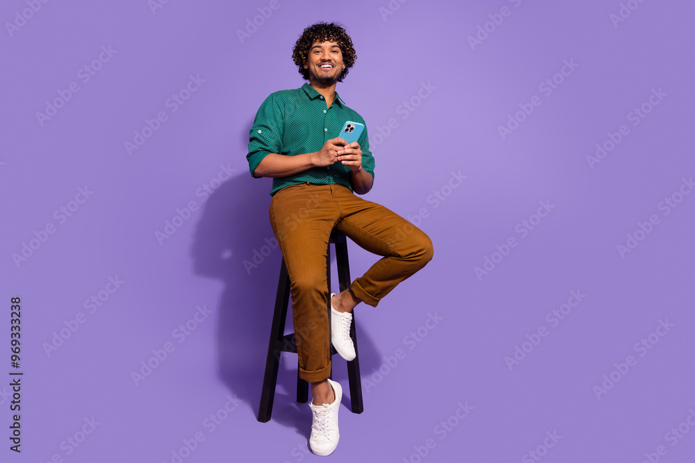 Wall mural Full body length photo of handsome mexican optimistic guy sitting stool with smartphone at his job isolated on violet color background