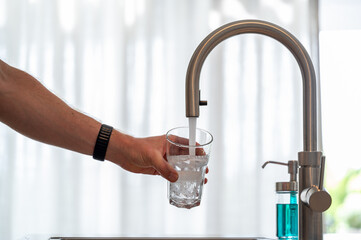 Man filling a glass of water in a modern kitchen.