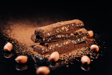 Chocolate bars with nuts and cocoa powder falling, captured in a stunning dark and reflective setup
