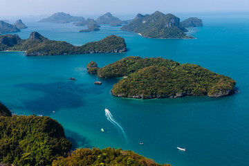 Fototapeta premium The beautiful landscape showcases turquoise waters surrounding dense green islands, with a small boat traversing the calm sea under a vibrant blue sky