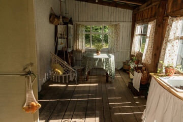 The warm light streams through the windows of a rustic wooden cottage, highlighting a simple dining table set with a plant. Vintage furnishings create a charming, welcoming atmosphere