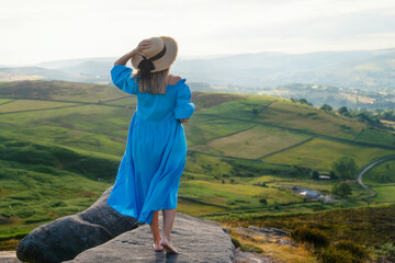 Woman in Blue Dress Gazes Over Lush Green Hills at Sunset in Serene Landscape