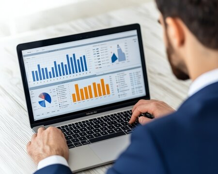 A businessman in a suit analyzes data and charts on his laptop.
