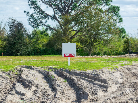 Street view of "Sold" sign on a vacant lot with recent tire ruts in sand in a suburban residential development on a sunny afternoon in southwest Florida. Motifs of real estate, commitment, the future.