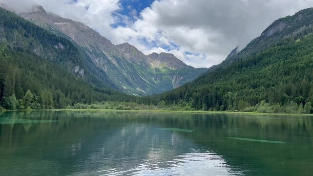 view of the Jagersee Lake with green mountains and cloud sky in the background in Kleinarl, Austria