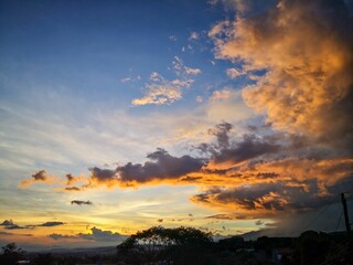 Obraz premium Vibrant sunset sky over landscape with silhouetted trees and mountains.
