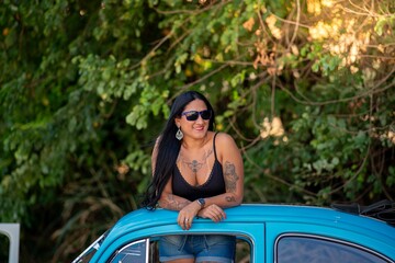 A woman with tattoos leaning out of a vintage blue car