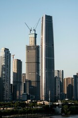 Fototapeta premium Skyscrapers in a city skyline with one under construction against a clear blue sky.