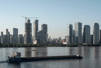 Fototapeta premium Cargo ship on river with city skyline