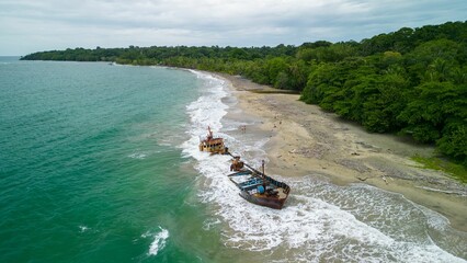 A shipwreck on a tropical beach with lush green forest and turquoise ocean waves in Manzanillo