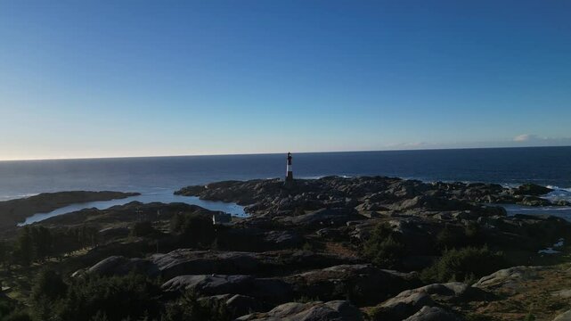 Drone scenery of Eigeroy Lighthouse on a rocky shore with blue sea and blue sky behind it in Norway