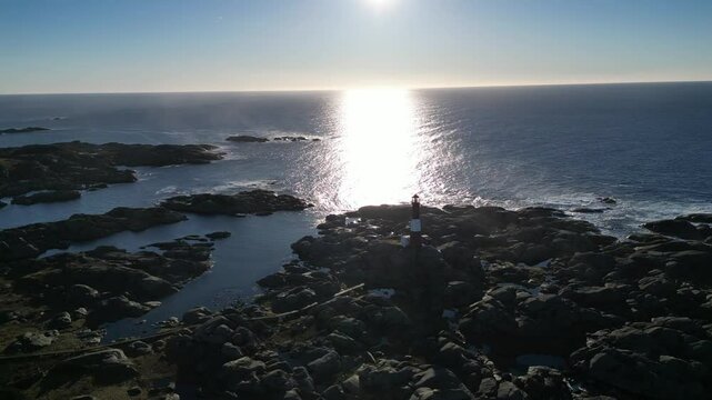 Drone of Eigeroy Lighthouse on a rocky shore with blue sea and blue sky behind it, at sunset, Norway