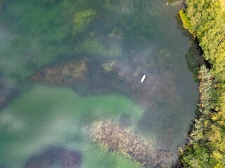 Aerial view of a paddleboarder on a clear green lake surrounded by lush vegetation.