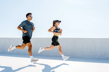 Two runners stride energetically under a bright sky, casting shadows as they move in perfect...