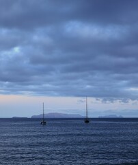 Fototapeta premium Sailboats on a calm sea with distant islands and a cloudy sky, Madeira Island, Portugal