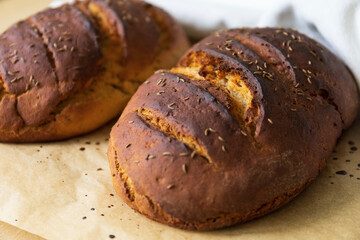 close up for two fresh baked rye bread loafs on a baking paper covered by a white towel