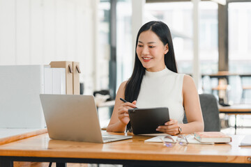 Asian businesswoman working on tablet and laptop in modern office space.
