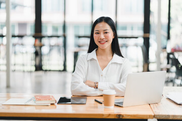 A confident woman in white shirt sits at desk with laptop, smiling warmly