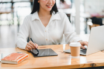 A woman using tablet and laptop in cozy workspace, enjoying her coffee