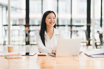 A professional woman smiles while working on laptop in modern office