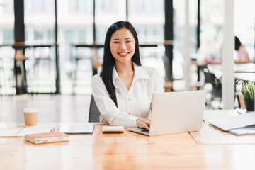 A professional woman smiles while working on laptop in modern office