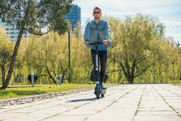 Man riding e-scooter in city public park at sunny summer day. Male driving electric scooter enjoying leisurely outdoor ride. Eco-friendly city transport and travel. Sustainable lifestyle concept