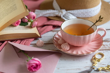 A cup of aromatic tea, a book and a rose on the table.