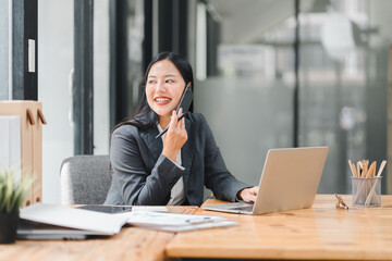 A professional woman smiles while working at her desk, engaged in phone call