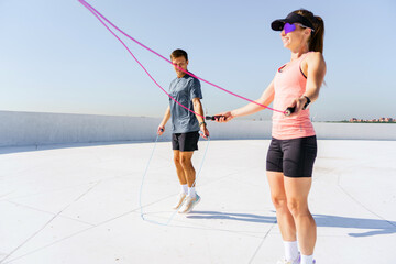 A man and a woman jump rope together outdoors, performing a synchronized cardio workout under a...