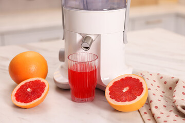 Modern juicer, fresh grapefruits and glass on white marble table in kitchen