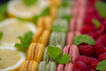 macaroons of different colors with with raspberries, lemon and mint
