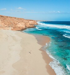 Aerial view of a person walking on a sandy beach with turquoise waters.