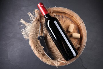 Sommelier knife with corkscrew, bottle of wine, corks and wooden barrel on grey table, top view