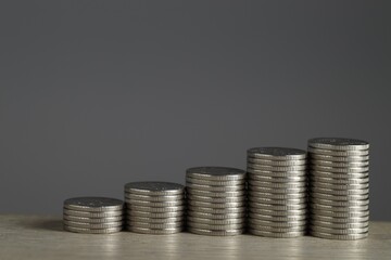 Stacked coins on wooden table against grey background, closeup with space for text. Salary concept